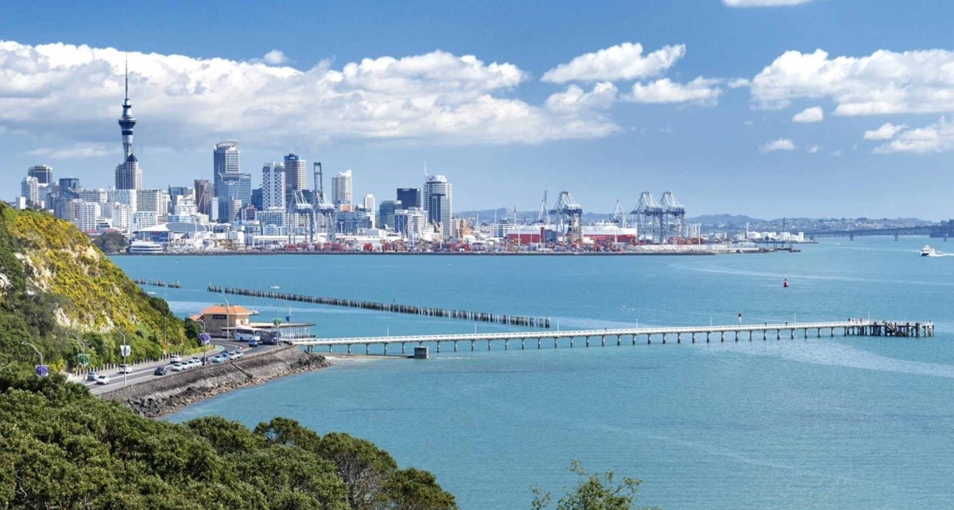 Backpacker looking at the Auckland skyline from a ferry during golden hour, symbolising the start of a New Zealand summer adventure.